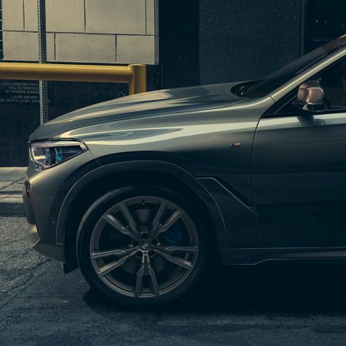 BMW X6 M50i in lateral perspective. Man leaning on BMW X6 M50i in lateral perspective in front of an urban setting.