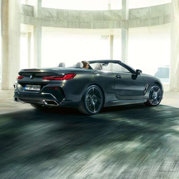 BMW M850i xDrive Convertible, three-quarter rear view. BMW M850i xDrive Convertible in Dravit Grey metallic with open softtop, three-quarter rear view, driving through concrete building.