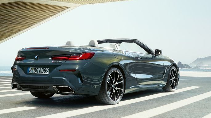 BMW M850i xDrive Convertible, three-quarter rear view. BMW M850i xDrive Convertible in Dravit Grey metallic with open softtop, three-quarter rear view, parking with ocean view.