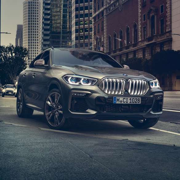 BMW X6 Adaptive M suspension Professional BMW X6 in three-quarter front perspective in front of an urban setting.