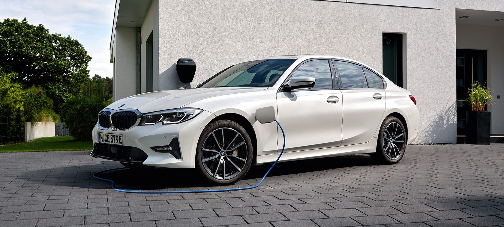 Plug-in hybrid BMW 3 Series Sedan 2021 G20 G20 three-quarter side view charging Plug-in hybrid BMW 3 Series Sedan 2021 G20 three-quarter side view charging in front of a garage