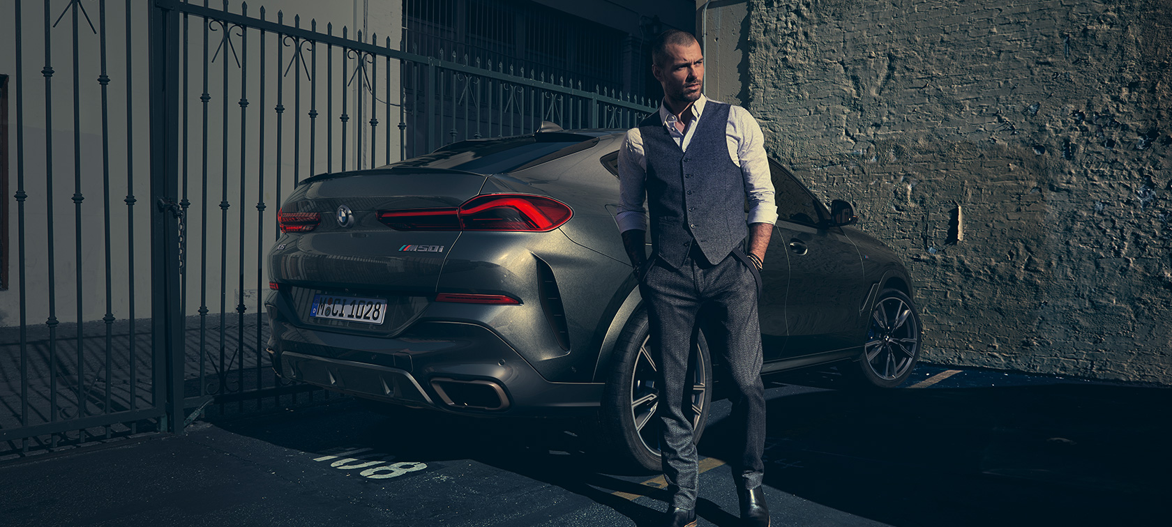 BMW X6 M50i in three-quarter rear view. Man standing next to BMW X6 M50i in three-quarter rear view.