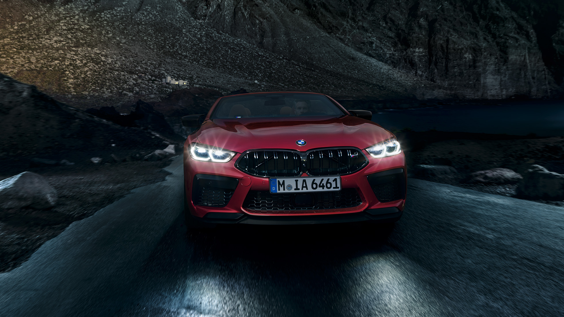BMW M8 Competition Convertible, front view. BMW M8 Competition Convertible in Motegi Red metallic with shining headlights, front view, driving at night.