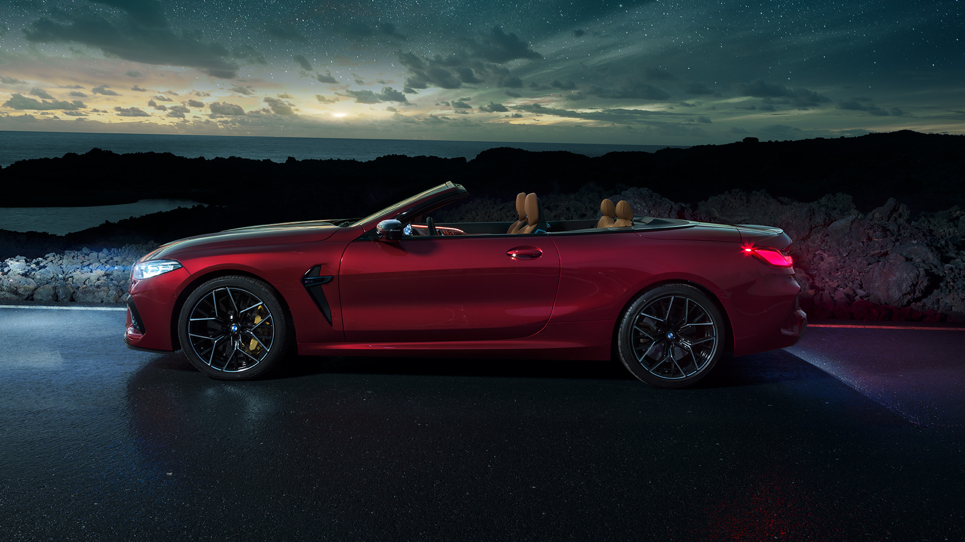 BMW M8 Competition Convertible, side view. BMW M8 Competition Convertible in Motegi Red metallic with open softtop, side view, standing at night under starry sky.