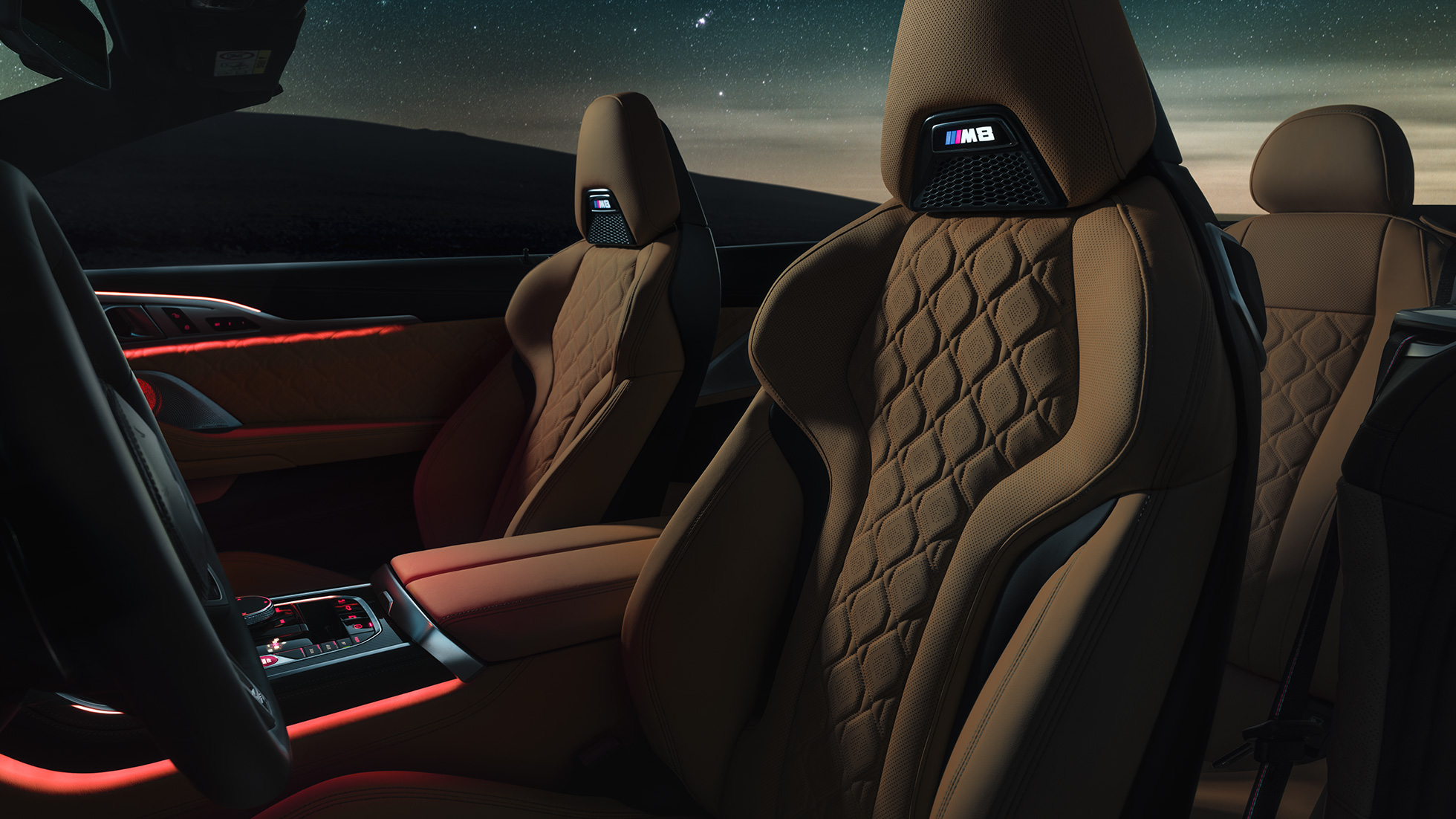 M Sport seats in leather 'Merino'. BMW M8 Competition Convertible with open softtop under starry sky, interior with M Sport seats in leather 'Merino' and red ambient light.