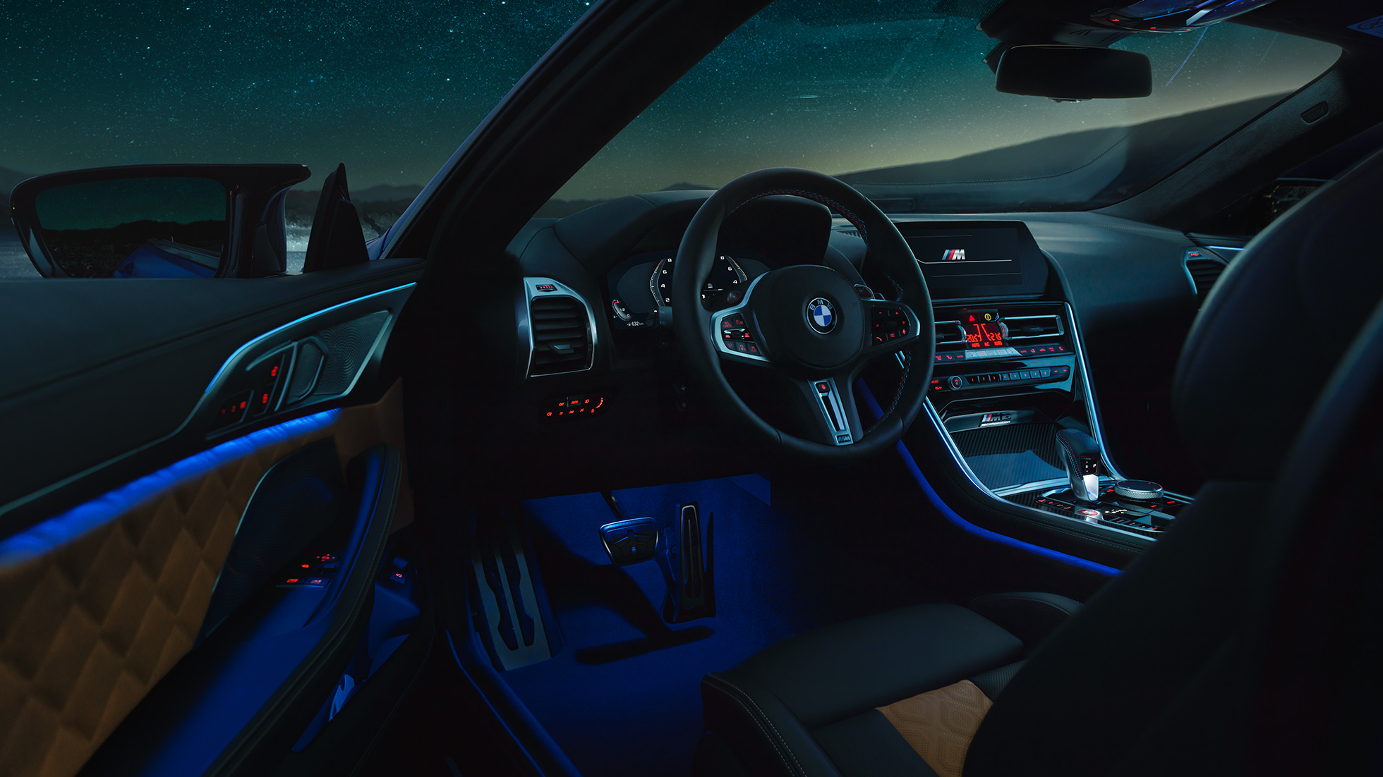 Interior BMW M8 Competition Coupé. BMW M8 Competition Coupé, interior at night with M leather steering wheel and blue ambient light with open driver door.