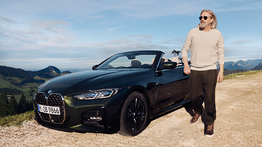 BMW Spring Summer Accessories Man walking next to a BMW in front of mountain landscape 